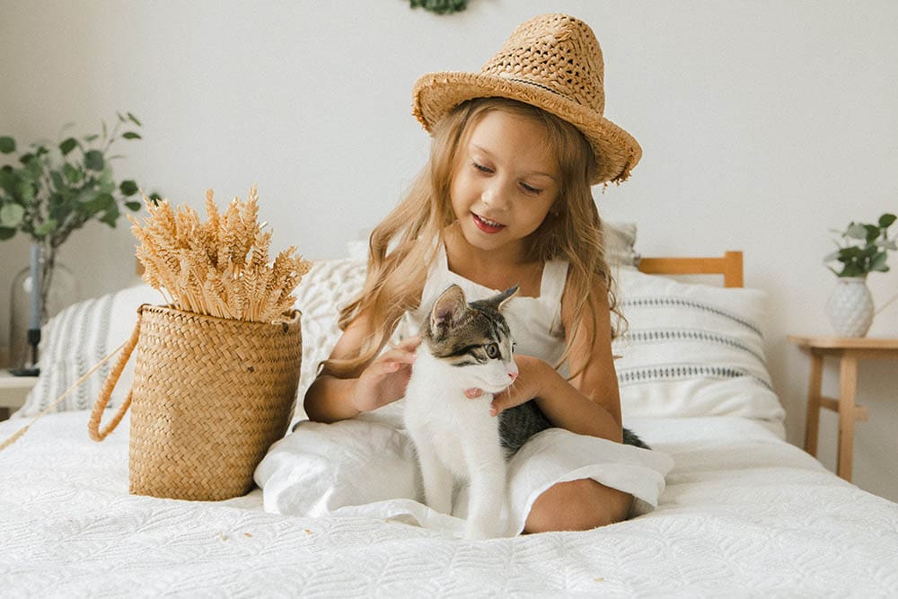 Счастливая девушка сидит на кровати и играет с кошкой