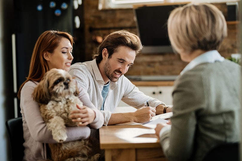 счастливый мужчина подписывает договор страхования домашних животных со своей женой и собакой на встрече с финансовым консультантом