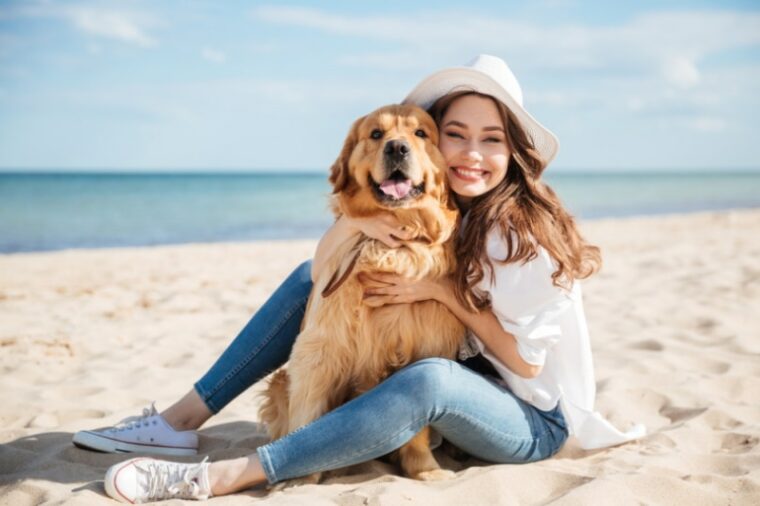 женщина обнимает свою собаку на пляже