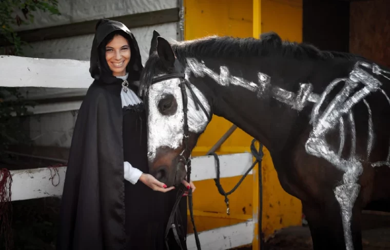 женщина в черном рядом с лошадью в нарисованном костюме скелета
